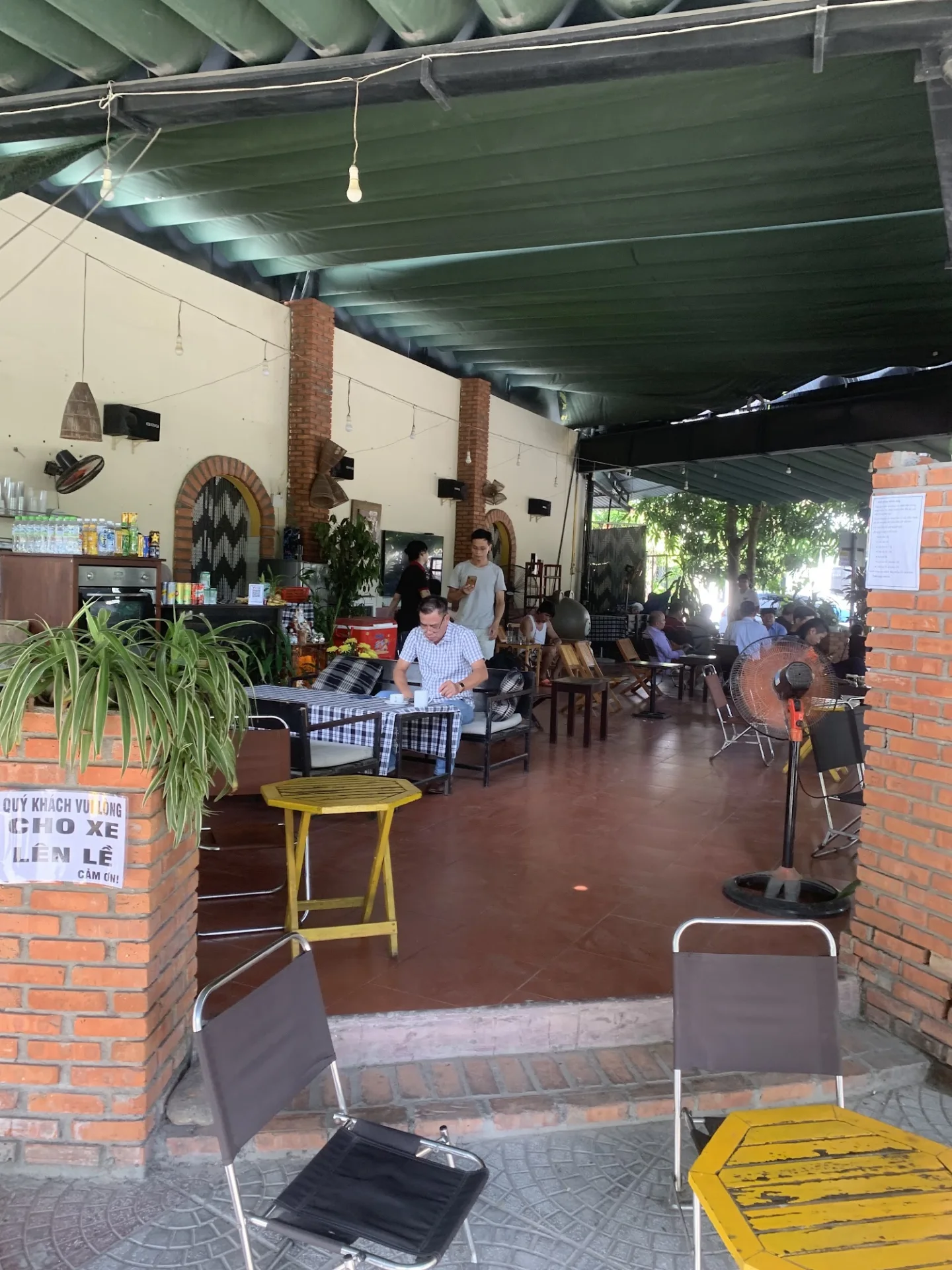 The real Cà Phê 89 interior, with brick pillars, green canopy and yellow tables